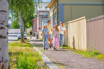 Perhe kävelemässä puutalokadulla