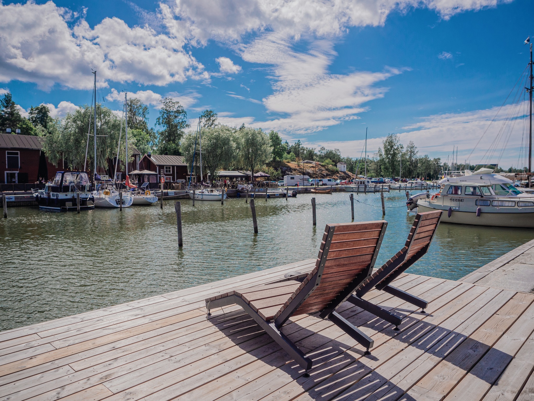 Kesäinen kaupunginlahti, puiset aurinkotuolit ja lahden toisella puolella punaiset, vanhat makasiinit.